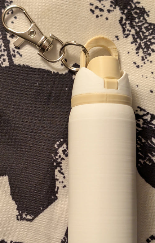 White bottle with beige accents and a keychain clip on a patterned background
