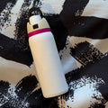 White cylindrical object with a pink band on a black and white patterned surface