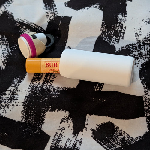 Burts Bees chapstick laying halfway inside a white bottle-shaped tube with the cap off 
