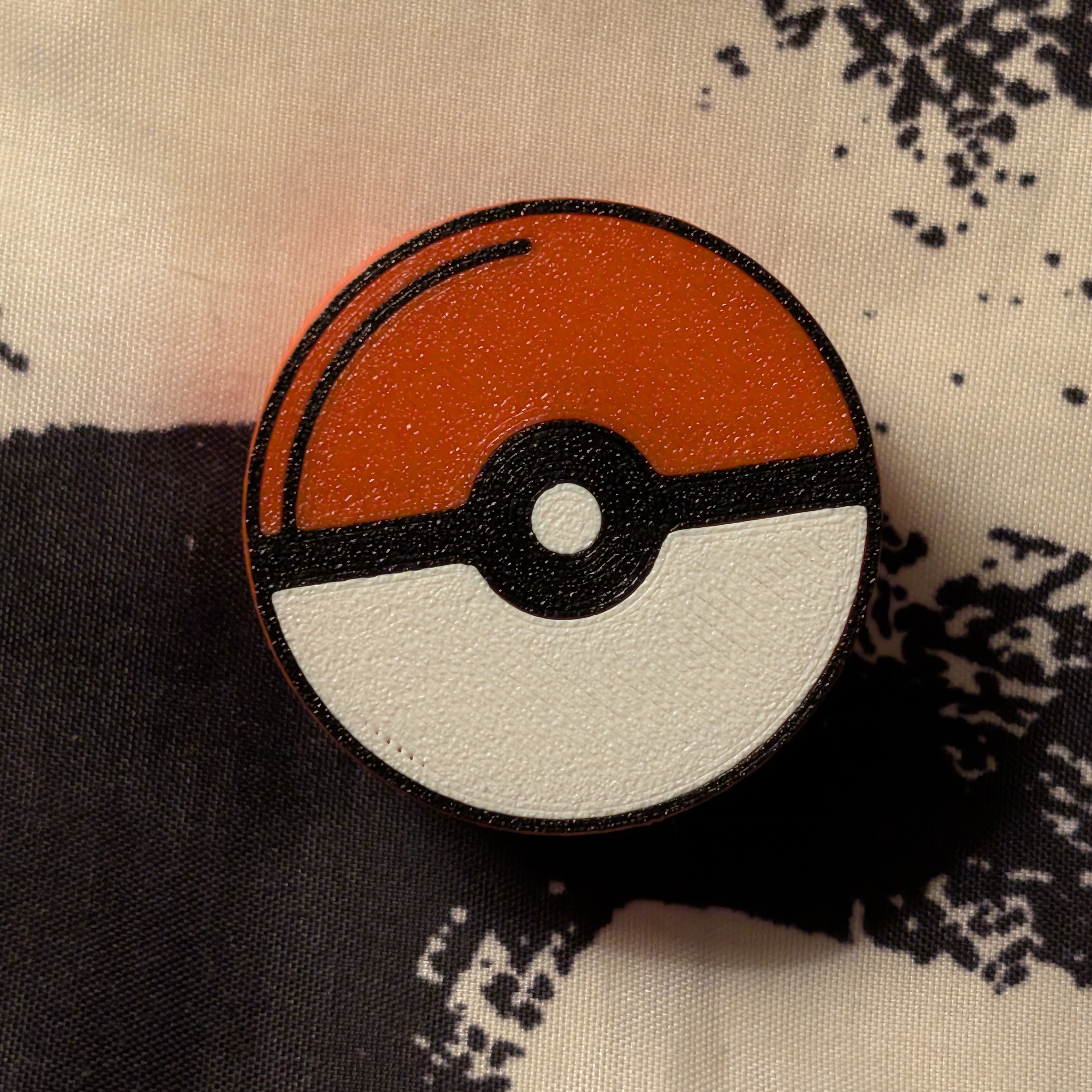 Red, white, and black pokeball decorative reel cover laying on black and white fabric